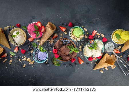 Various colorful ice cream balls in different bowls, with ice cream waffles cones and flavor ingredients - pistachio nuts, berries, lemon, chocolates, vanilla beans, mint. Dark background copy space