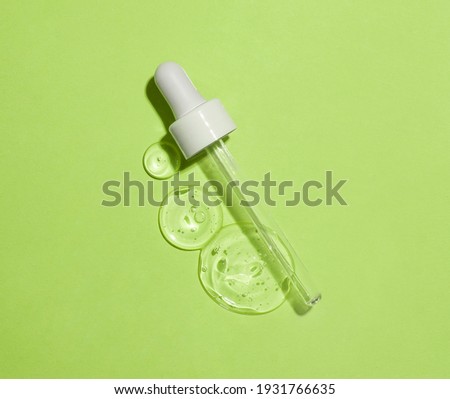 Face serum drops with cosmetic pipette on green background. Flat lay.