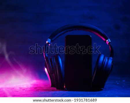 Wireless over-ear headphones on the desk, neon style. Empty smartphone with space for text