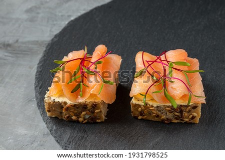 Healthy sandwiches with microgreens - cereal bread toasts with smoked salmon, creamy cheese and beetroot sprouts on a gray background
