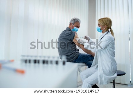 An elderly man getting vaccine shot by doctor epidemiologist in hospital office during corona virus pandemic. Immunization of older population. Royalty-Free Stock Photo #1931814917