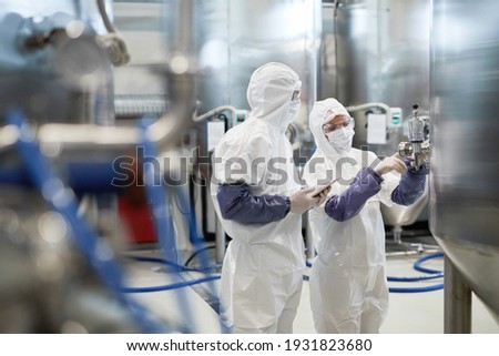 Side view portrait of two workers wearing protective suits while using equipment at modern chemical plant, copy space Royalty-Free Stock Photo #1931823680