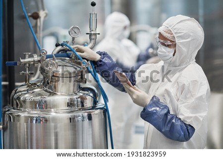 Portrait of female worker wearing protective suit while operating equipment at modern chemical plant, copy space Royalty-Free Stock Photo #1931823959