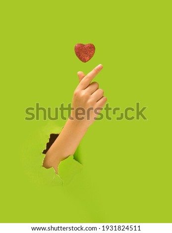 K pop concept. A girl hand showing fingers heart gesture. Red glittery heart above. Bright green in background.