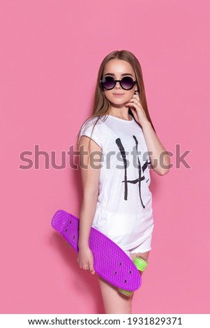 Cheerful young girl with a skateboard on the pink background.