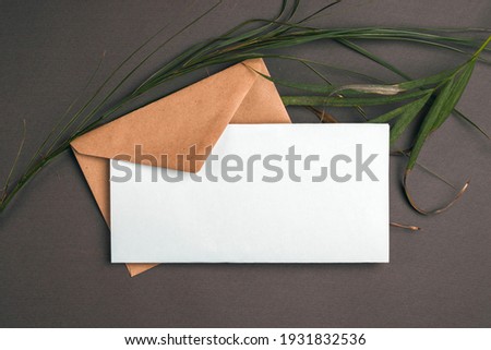 Blank white sheet and vintage envelope mockup on gray background with dry palm leaves. Flat lay, top view.