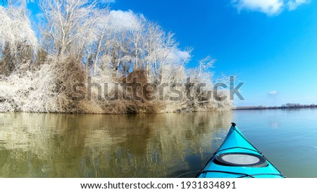 View from bow of blue kayak on frosty winter trees by the Danube river