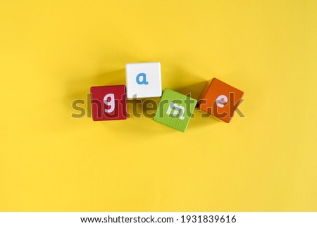 GAME - Word made from colored wooden blocks. Painted cubes with letters on yellow background. Top view. Selective focus. Copy space.
