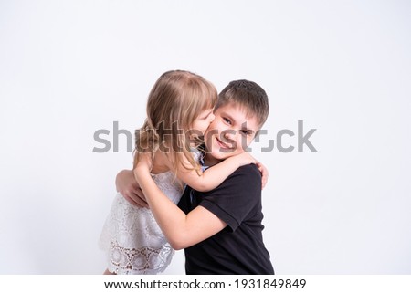 cute little sister kissing hugging her handsome older brother teenager on white background.