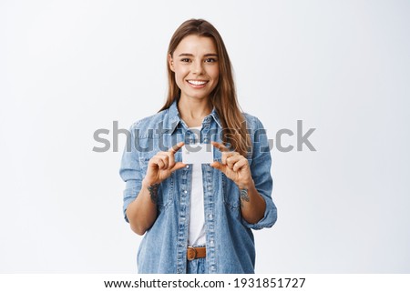 Portrait of young woman recommending bank, showing plastic credit card over chest and smiling, giving advice for deposit, standing against white background