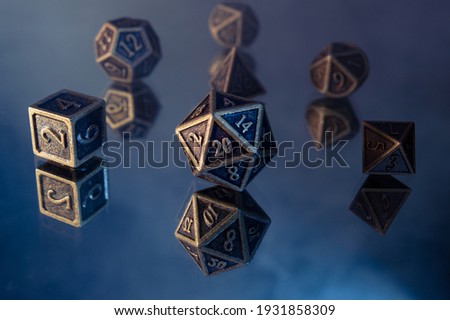 Close-up photo of a set of bronze rpg dice on a reflective surface showing their mirror images. Focused on the 20-sided die in the front while the four other dice dissolve in the smoke background