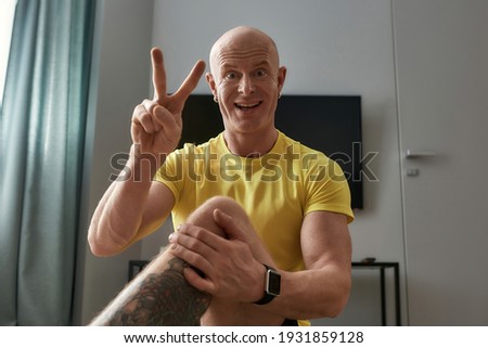 Online workout. Mature personal fitness trainer gesturing at camera and smiling while conducting virtual fitness class at home. Sport and healthy lifestyle