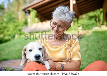 Portrait of senior woman sitting outdoors in garden, pet dog friendship. Royalty-Free Stock Photo #1931860376