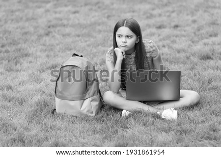 sad teen girl using notebook for online education and learning sitting in park on green grass with backpack, back to school.