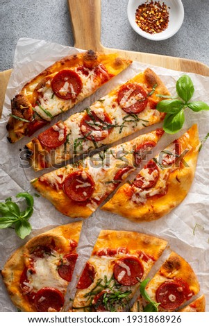 Flatbread pepperoni pizza topped with fresh basil sliced, top view Royalty-Free Stock Photo #1931868926