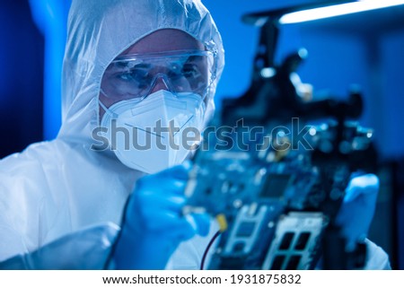 Microelectronics engineer works in a modern scientific laboratory on computing systems and microprocessors. Electronic factory worker is testing the motherboard and coding the firmware. Royalty-Free Stock Photo #1931875832