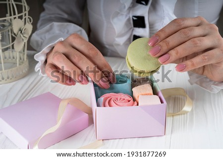Female hands unpack a small box with macaroon and marshmallow 