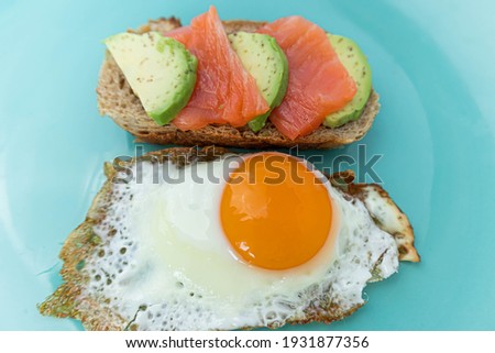 Homemade toast sandwich with salmon and avocado on a slice of cereal bread. Fried eggs with bright yolk on a mint background