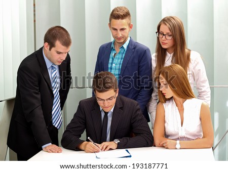 Confident businessman signing the contract in front of his team