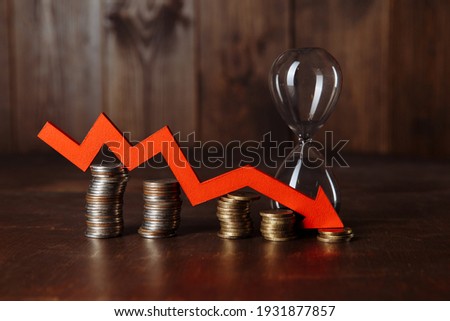 Red down arrow on stacks of gold coins and hourglass. Investment and savings