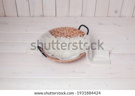 Wicker basket on a wooden background. Photo zone for taking pictures of a newborn baby. White fur, winding. Preparing for a photo session. Photoshoot. Props. Newborn nest. 