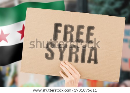 The phrase " Free Syria " on a banner in men's hand with blurred Syrian flag on the background. Protest. Riot. Violence. Economic crisis. Collapse. Politics. Streets. Save. Cruelty