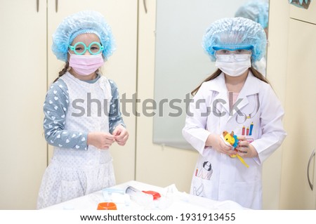 Two cute girls dressed as doctors treat toys in a children's makeshift toy hospital, children play pediatricians during the coronavirus quarantine.
