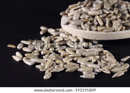 close up of sunflower seeds without shell on a wooden spoon, over black background