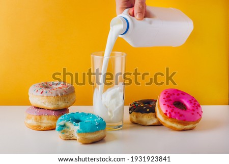 Colorful donuts with chocolate, peanut butter, and jam filling. Man hand pouring plant milk into the glass. Sweet tooth home breakfast for text copy