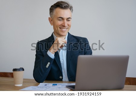 Smiling middle aged freelancer working from home. Handsome mature businessman using laptop computer planning project, searching online sitting in office. Successful business 