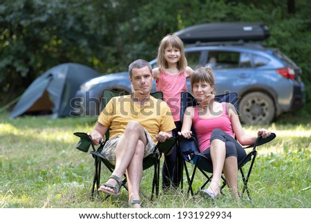 Happy young family parents and their daughter resting together at camping site in summer.