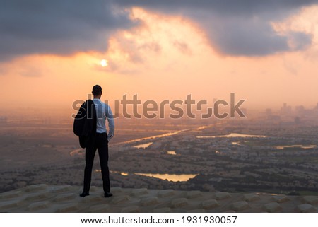 Calm business man standing above on rooftop looking at the city view at sunset.  Royalty-Free Stock Photo #1931930057