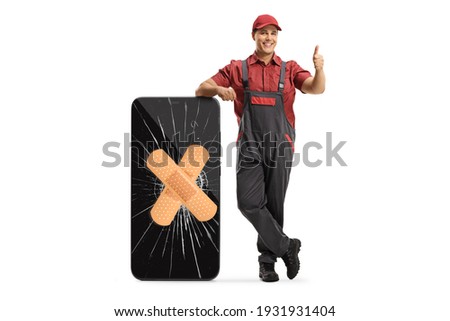 Technician leaning on a smartphone with a cracked screen and bandage and gesturing a thumb up sign isolated on white background
