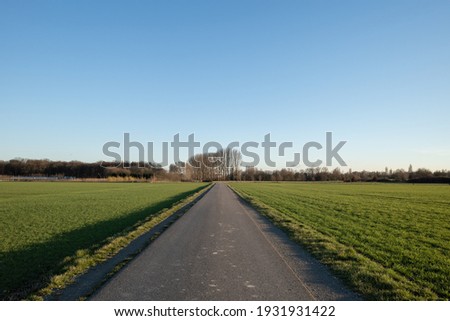 Diminishing perspective view of tranquil street between agricultural field on countryside area in Germany against blue sky.  Royalty-Free Stock Photo #1931931422