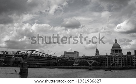 Black and white photo of a gloomy, cloudy London skyline, including a famous cathedral and bridge, over the River Thames