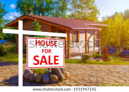 Private house for sale. House for sale sign on the background of a blurry image of a cottage. Buying and selling real estate. Rural properties. Sale of houses in rural areas.