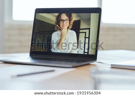 Cheerful female teacher smiling at camera during video call, having online lesson with schoolchildren studying from home. Focus on laptop screen