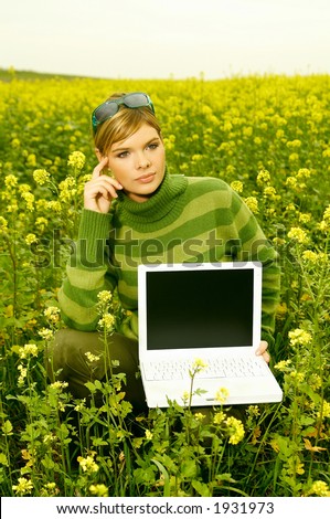 Young business woman with laptop computer on green meadow full of yellow flowers