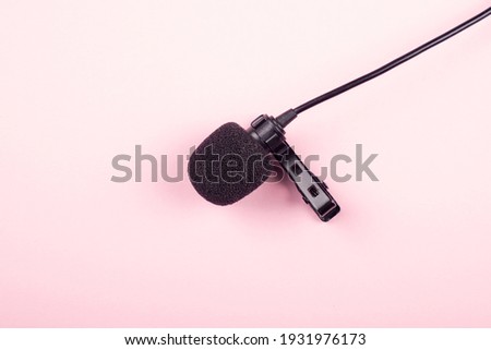 black lavalier microphone close-up on pink background.