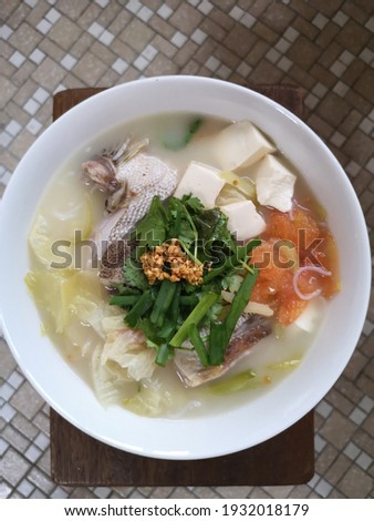 Homecook grouper fish head noodles. Putting in tofu, tomatoes, salted vegetables, bok choy into the soup and topped with spring onions, parsley leaves and fried garlic to enhance the taste of the soup