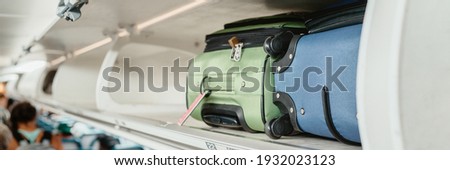 Carry-on luggages in overhead compartment of plane for international flights. Travel restrictions during coronavirus not allowing hand baggage inside airplane. Royalty-Free Stock Photo #1932023123