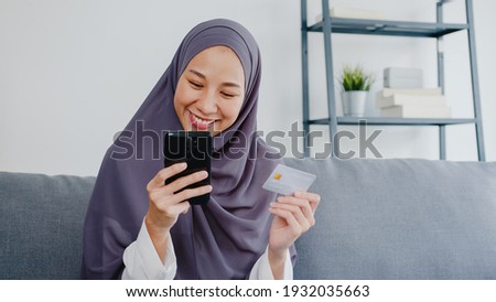 Asia muslim lady use smart phone, credit card buy and purchase e-commerce internet in living room at house. Stay at home, online shopping, self isolation, social distance, quarantine for coronavirus.