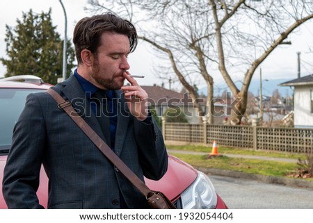 Caucasian man in his thirties smoking a cigarette in front of a red car