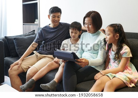 Asian family resting in sofa at home and watching cartoon or movie on tablet computer