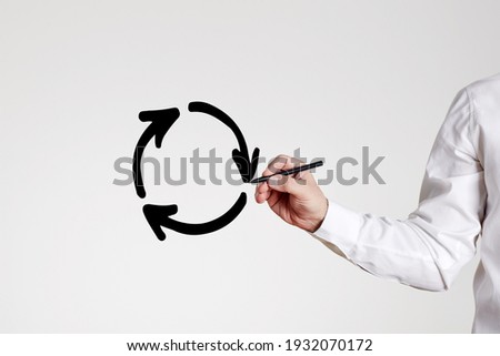 Businessman draws a recycling circle with arrows on gray background. Business or economic stagnation or recycle concept.

 Royalty-Free Stock Photo #1932070172