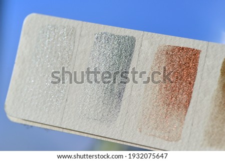Fragment of a color palette with metallic colors of watercolor paints. Blue background, watercolor paper, glitters in the sun.