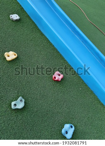 the colorful icons of climbing facilities with green artificial turf and blue slide for children in the park design for adventure concept close-up	