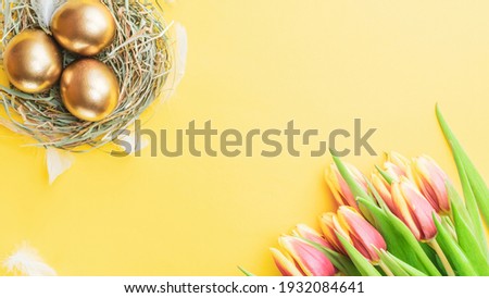 Easter eggs Golden color in basket with spring tulips, white feathers on pastel yellow background in Happy Easter decoration. Festive decoration in flat lay