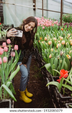 Woman gardener makes selfie. The girl smiles and uses a mobile phone in the tulip flowers greenhouse. Soft selective focus.