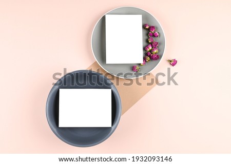 Blank white paper card on gray plate, pink pastel surface with rosebuds. Mock-up of blank greeting card. Minimal business brand template. Flat lay, top view. High quality photo
